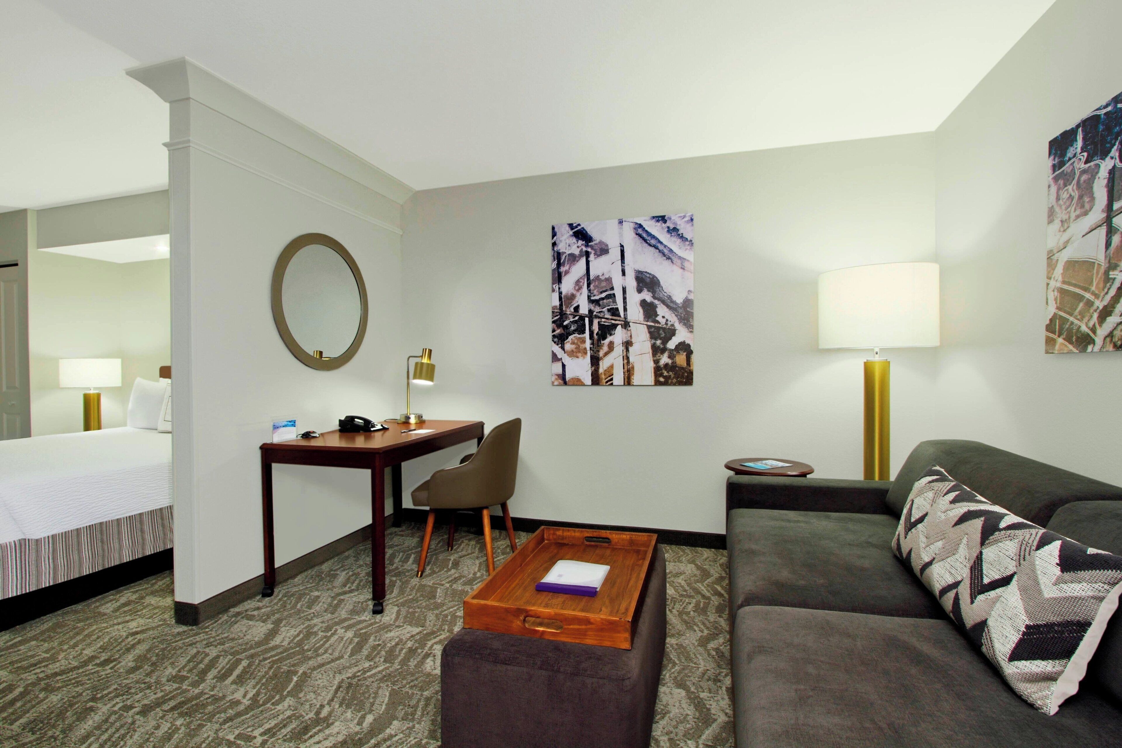 A hotel room with a bed, a desk with a lamp, a chair, a sofa, and a coffee table.