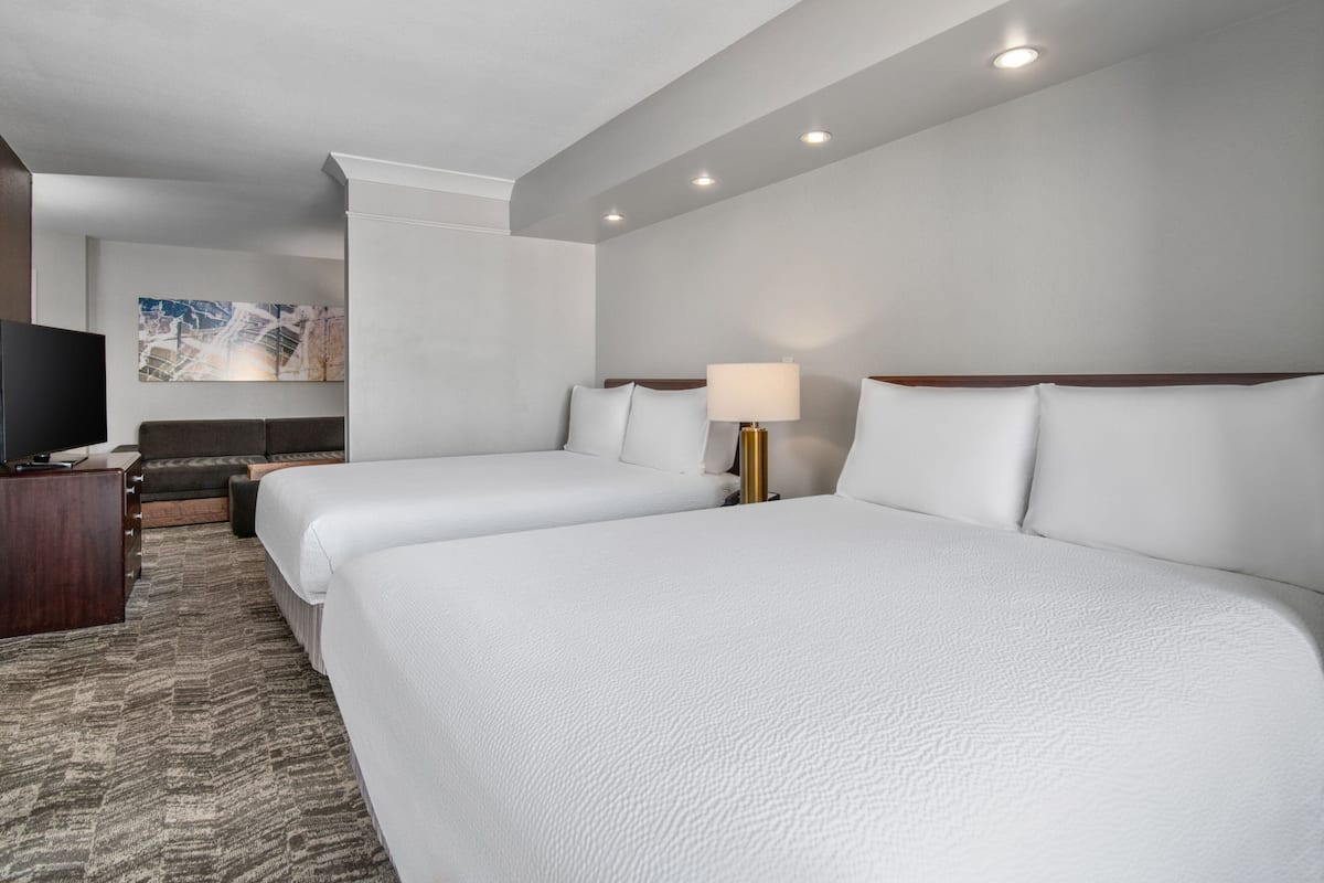 A hotel room with two beds, a desk, a television, and a painting on the wall.