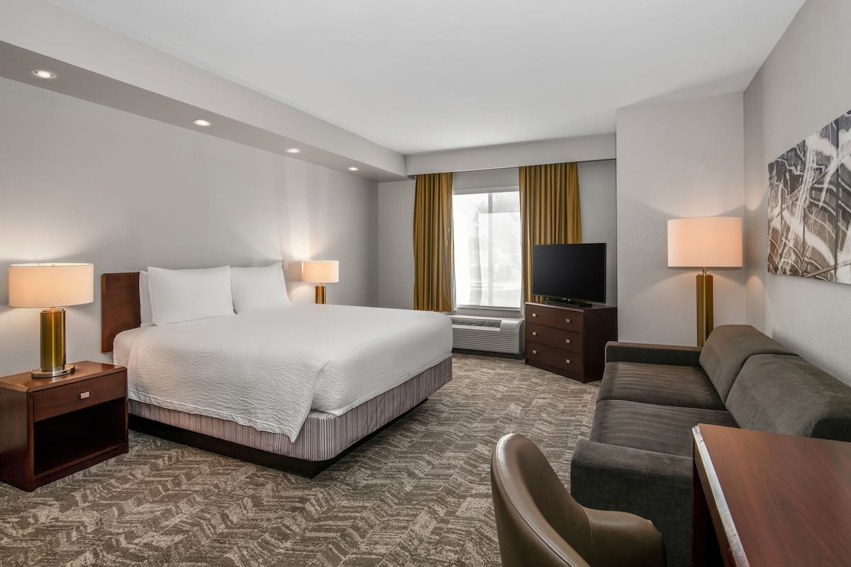 A hotel room with a large bed, a TV, a sofa, and a desk.