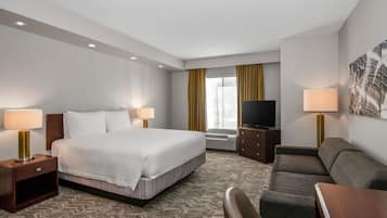 A hotel room with a large bed, a TV, a sofa, and a desk.
