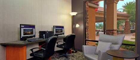 A hotel room with two computer desks, two chairs, a small table, and a large window offering a view of the outside.