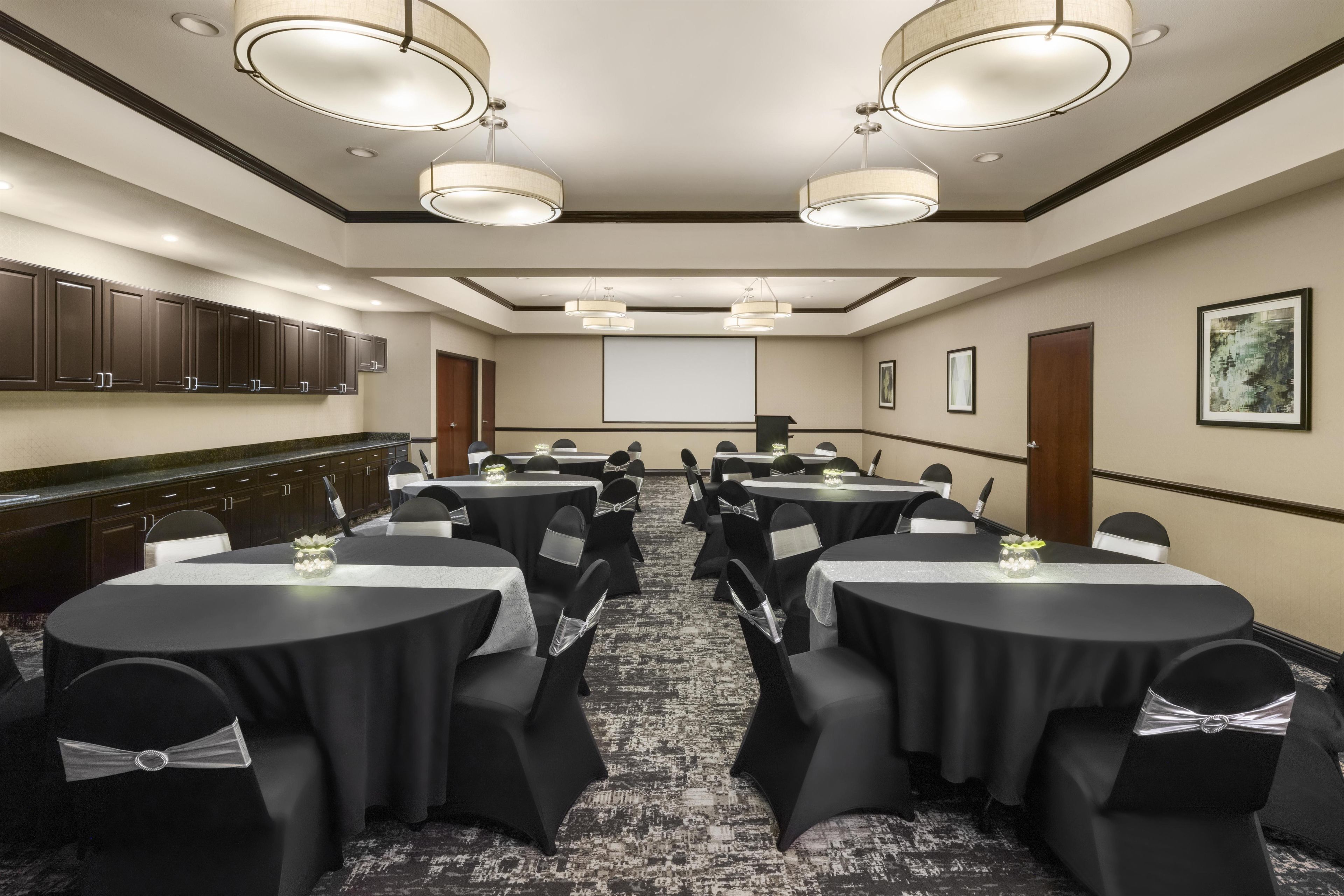 A conference room with round tables, chairs, and a projector screen.