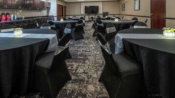 A conference room with multiple tables and chairs, equipped with a projector screen and a television.