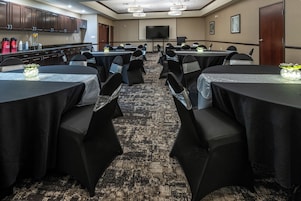 A conference room with multiple tables and chairs, equipped with a projector screen and a television.