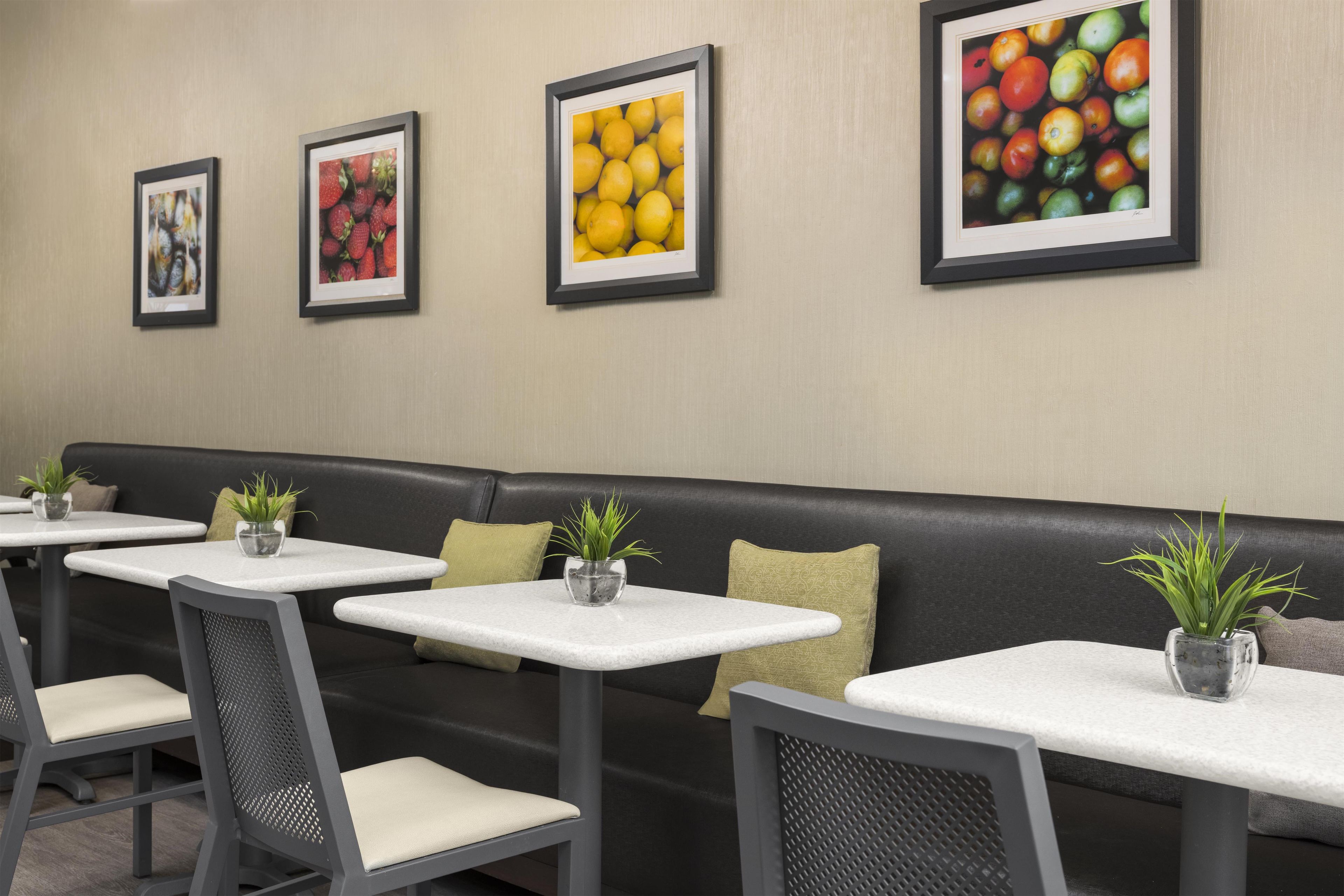 A seating area with a black leather bench, white tables, and chairs, each with a small potted plant.