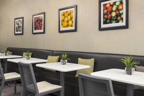 A seating area with a black leather bench, white tables, and chairs, each with a small potted plant. - Best Western Plus Duncanville/Dallas (Duncanville)