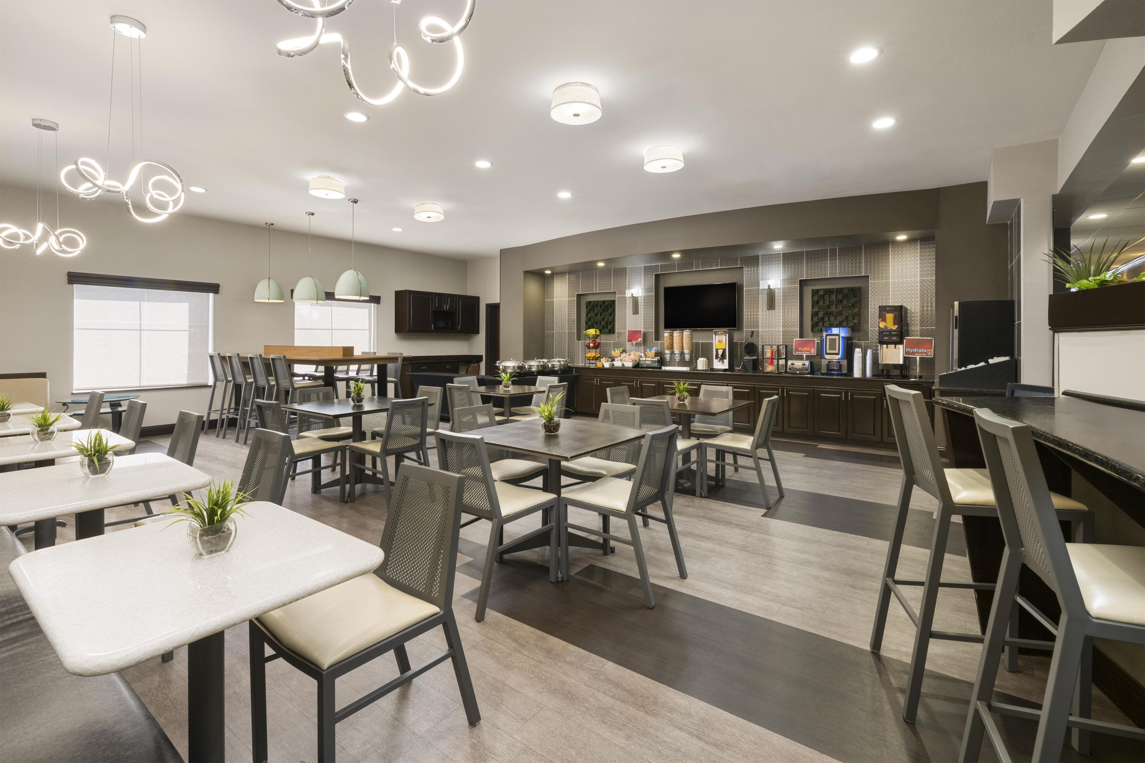 A modern dining area with tables and chairs, a kitchen area with a bar, and a television mounted on the wall.