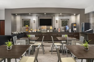 Restaurante moderno com televisão de tela plana, estação de autoatendimento para bebidas e diversas opções de comida.