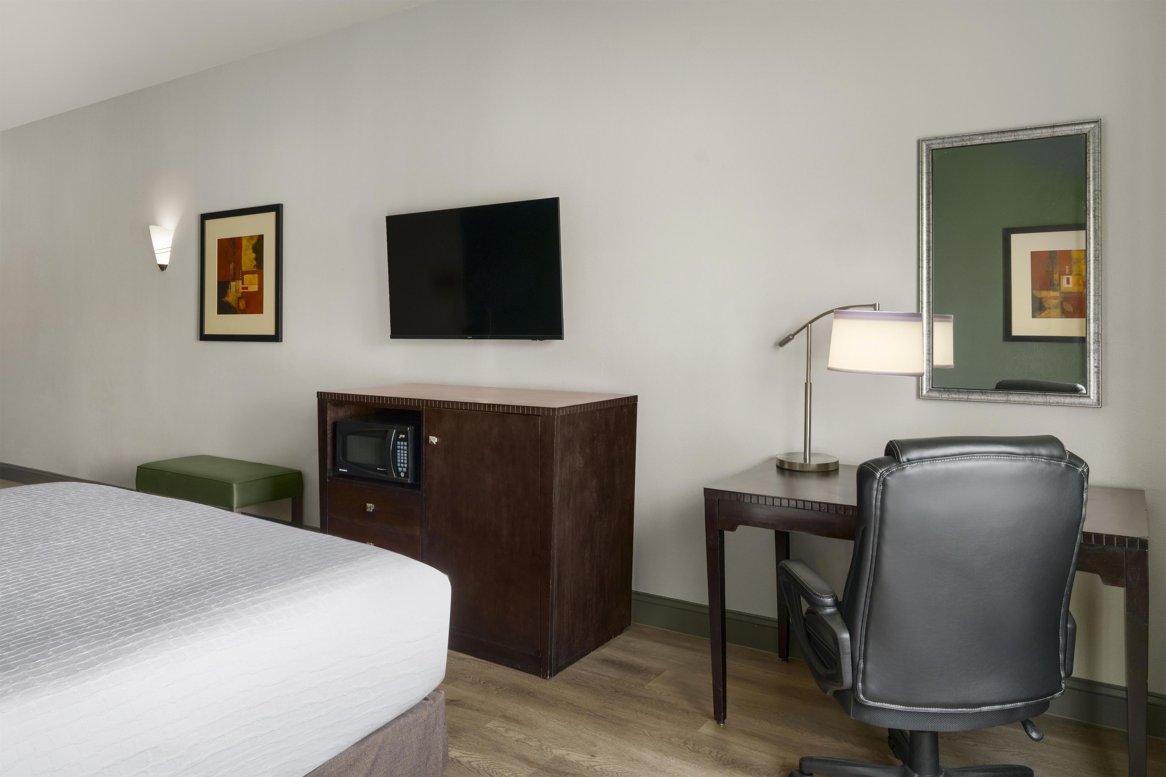 Ein Hotelzimmer mit einem Bett, einem Schreibtisch mit Stuhl, einem Fernseher, einer Schreibtischlampe und einem Spiegel.