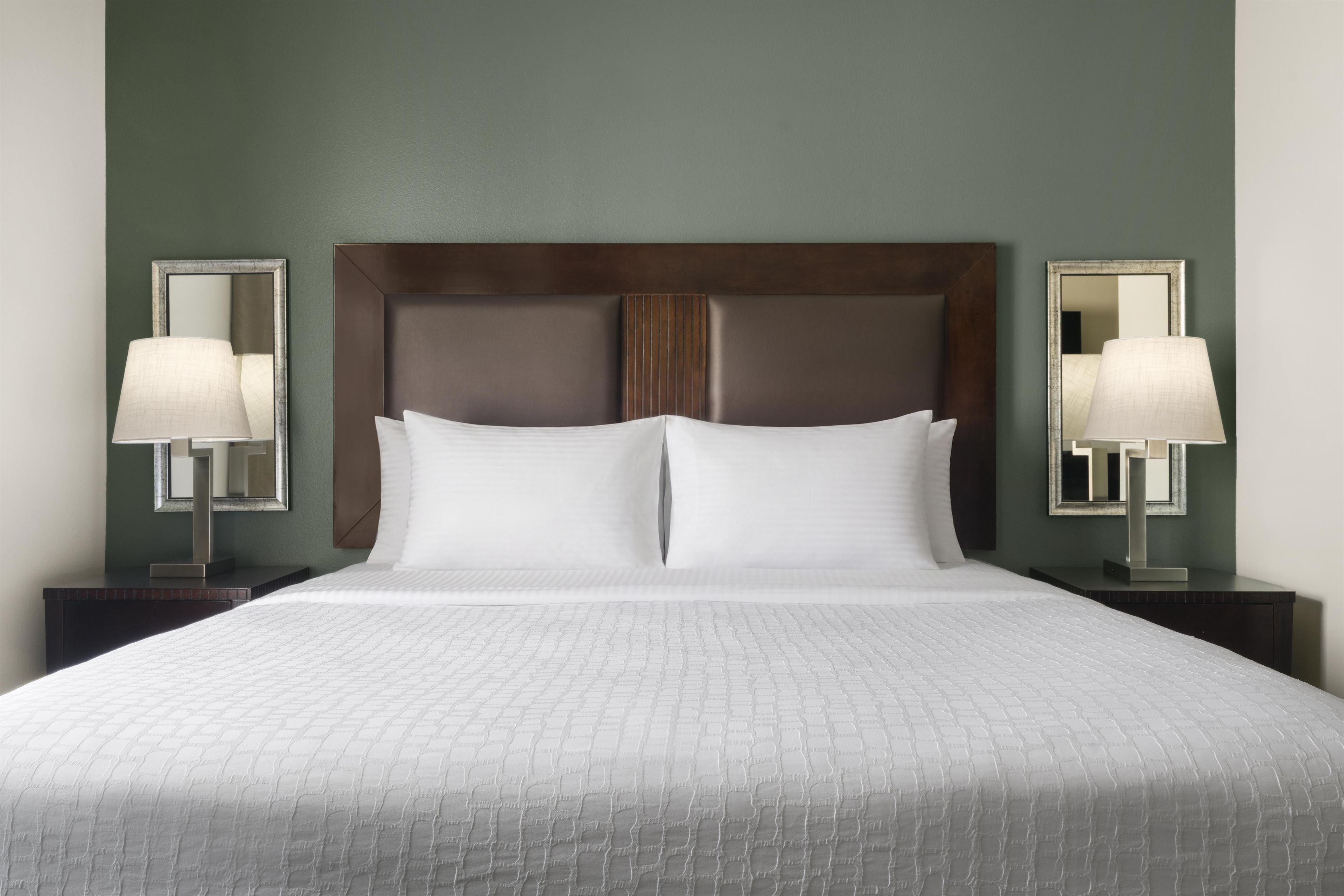 A standard hotel room with a large bed, two bedside tables, and two wall-mounted lamps.