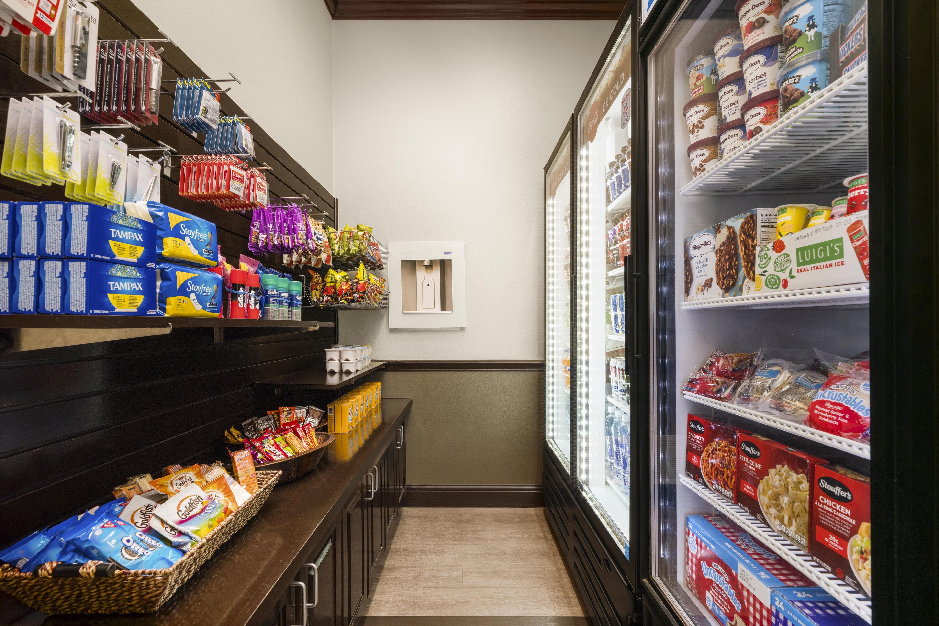 A grocery store aisle with shelves stocked with various products including Tampax, Goldfish, and ice cream.