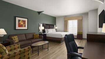Habitación de hotel con cama, sofá, sillón, mesita y un cuadro en la pared.