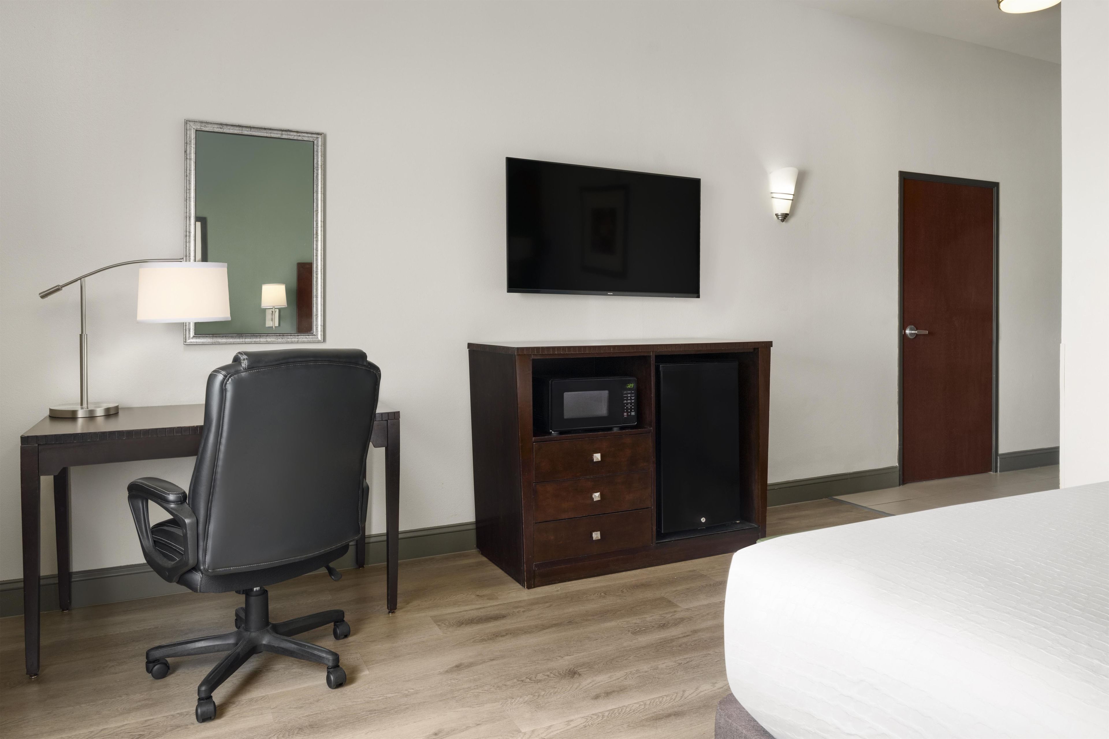 A hotel room with a bed, a desk with a chair, a television, a microwave, a dresser, and a door.