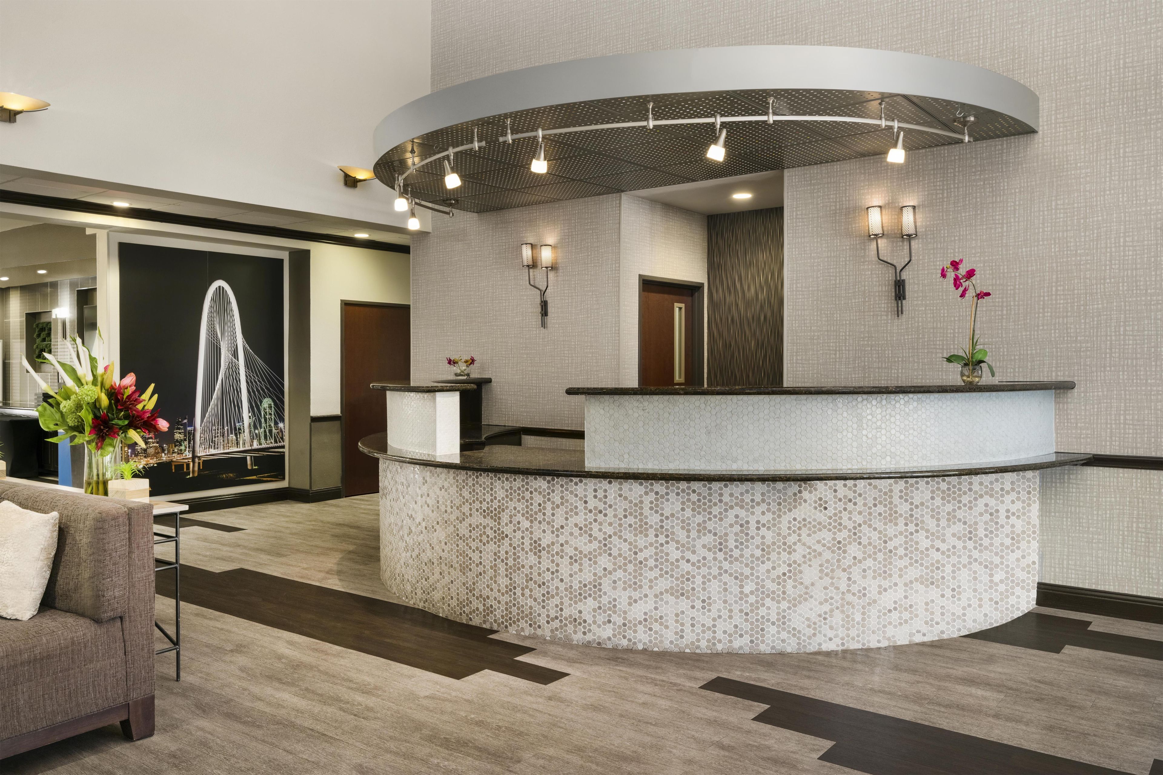 A reception area with a curved counter, a wall-mounted light fixture, and a decorative vase with flowers.