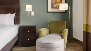 A hotel room with a bed, a nightstand, a lamp, a chair, and a framed artwork on the wall. - Best Western Plus Duncanville/Dallas (Duncanville)