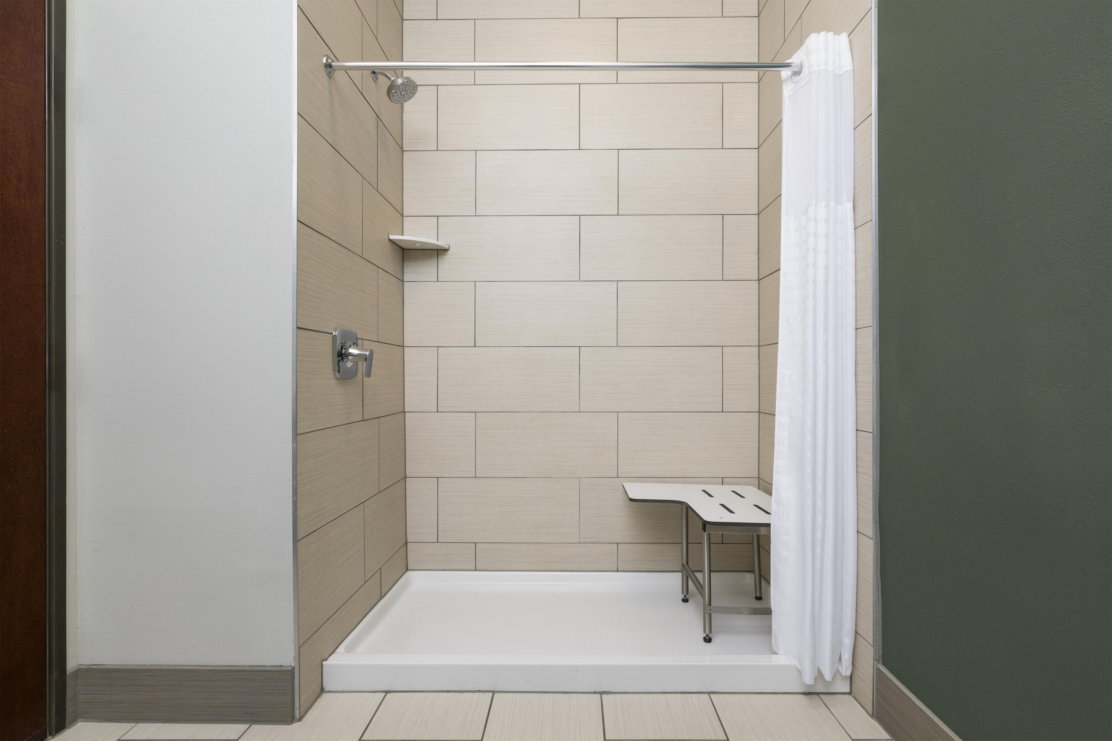 A walk-in shower with a white floor, a showerhead, and a white curtain.
