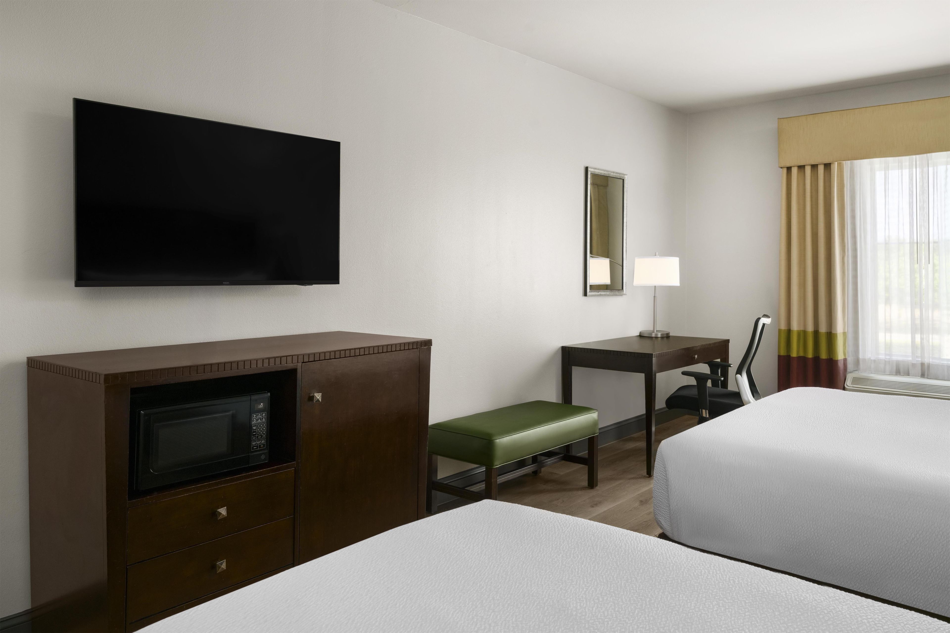 Een hotelkamer met twee bedden, een bureau, een televisie, een magnetron en een raam met gordijnen.