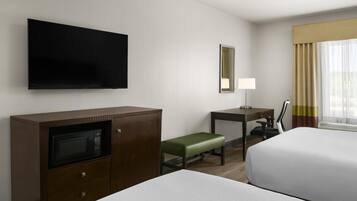 A hotel room with two beds, a desk, a television, a microwave, and a window with curtains.