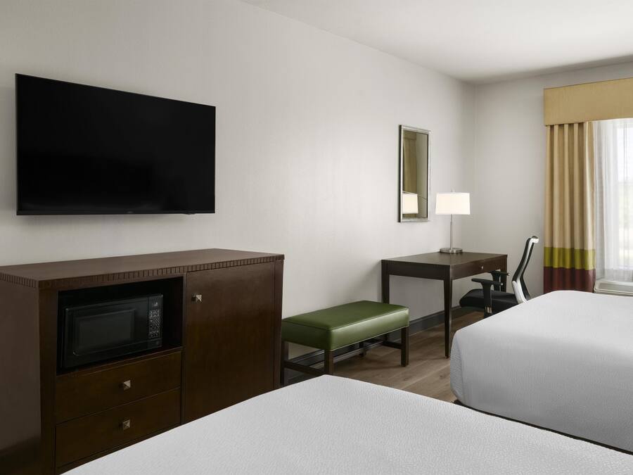 A hotel room with two beds, a desk, a television, a microwave, and a window with curtains.