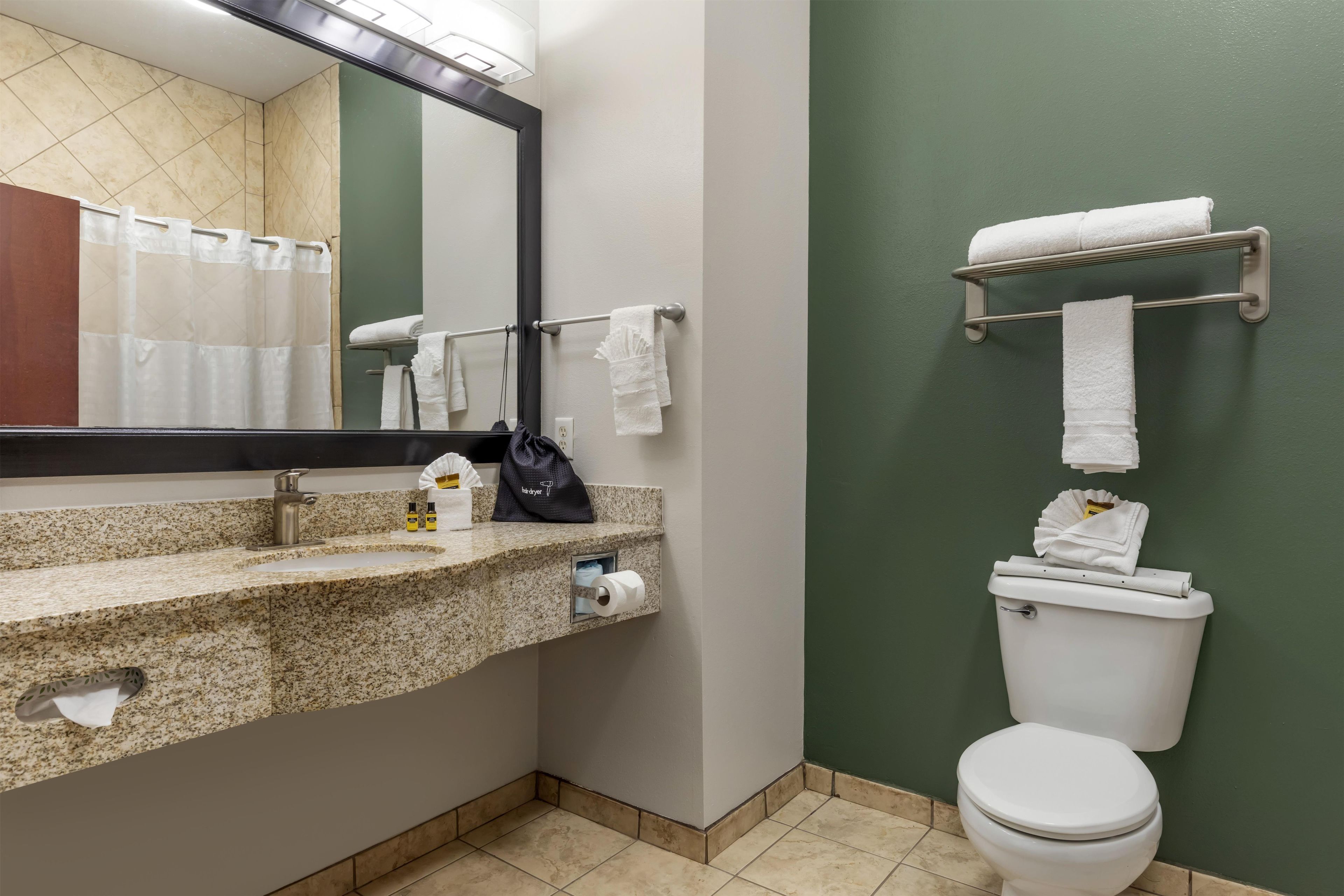 Un baño con encimera de granito, un espejo, toallero, inodoro y dispensador de toallas de papel.
