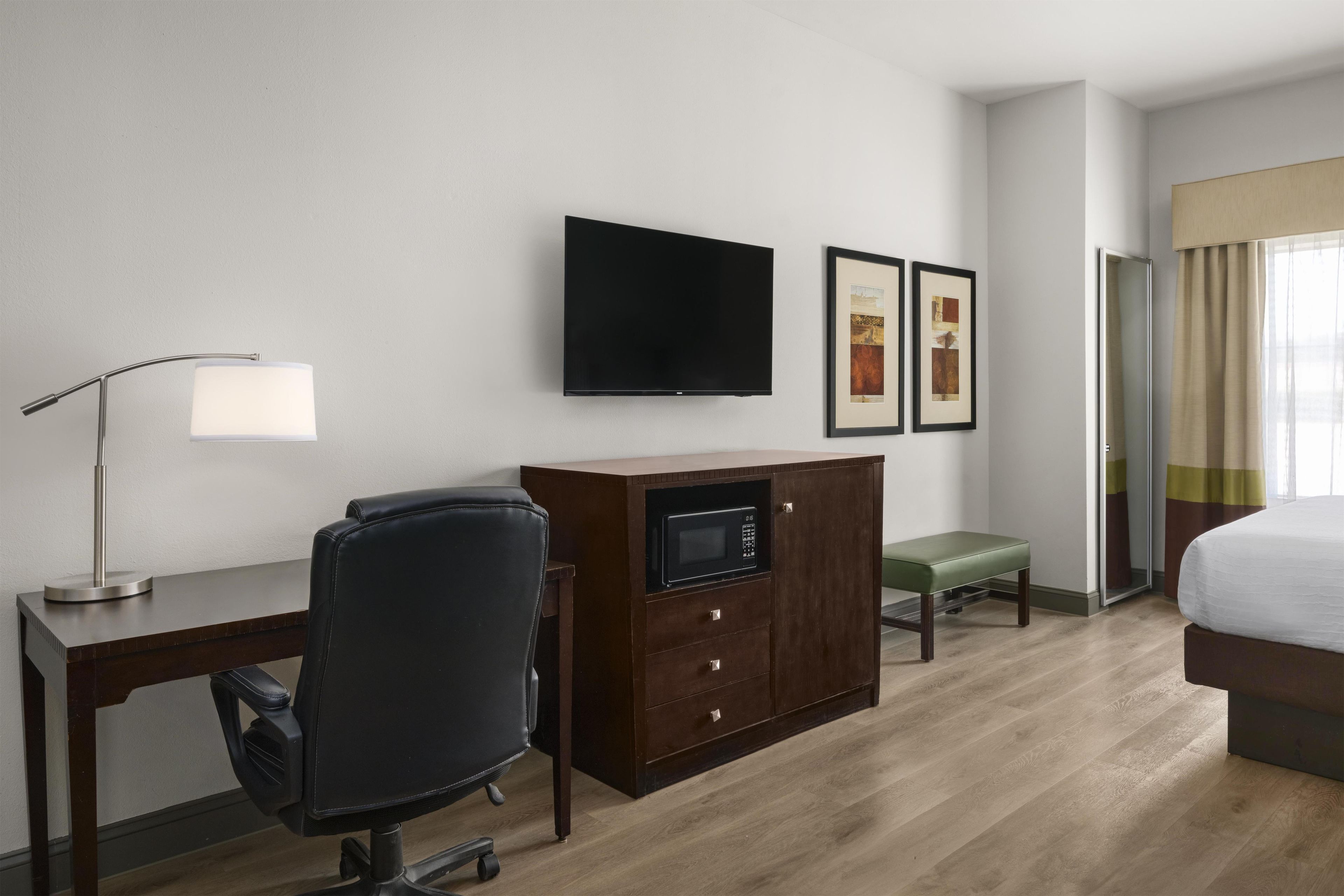 A hotel room with a desk, chair, flat-screen TV, artwork, and a bed.