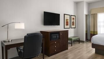 A hotel room with a desk, chair, flat-screen TV, artwork, and a bed.