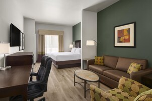 Quarto de hotel com cama, escrivaninha, poltrona, sofá, mesa pequena e luminária.