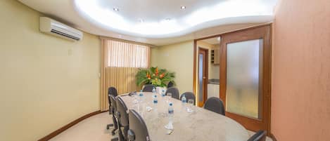 A conference room with a curved ceiling, recessed lighting, a long table with chairs, a potted plant, and a frosted glass door.