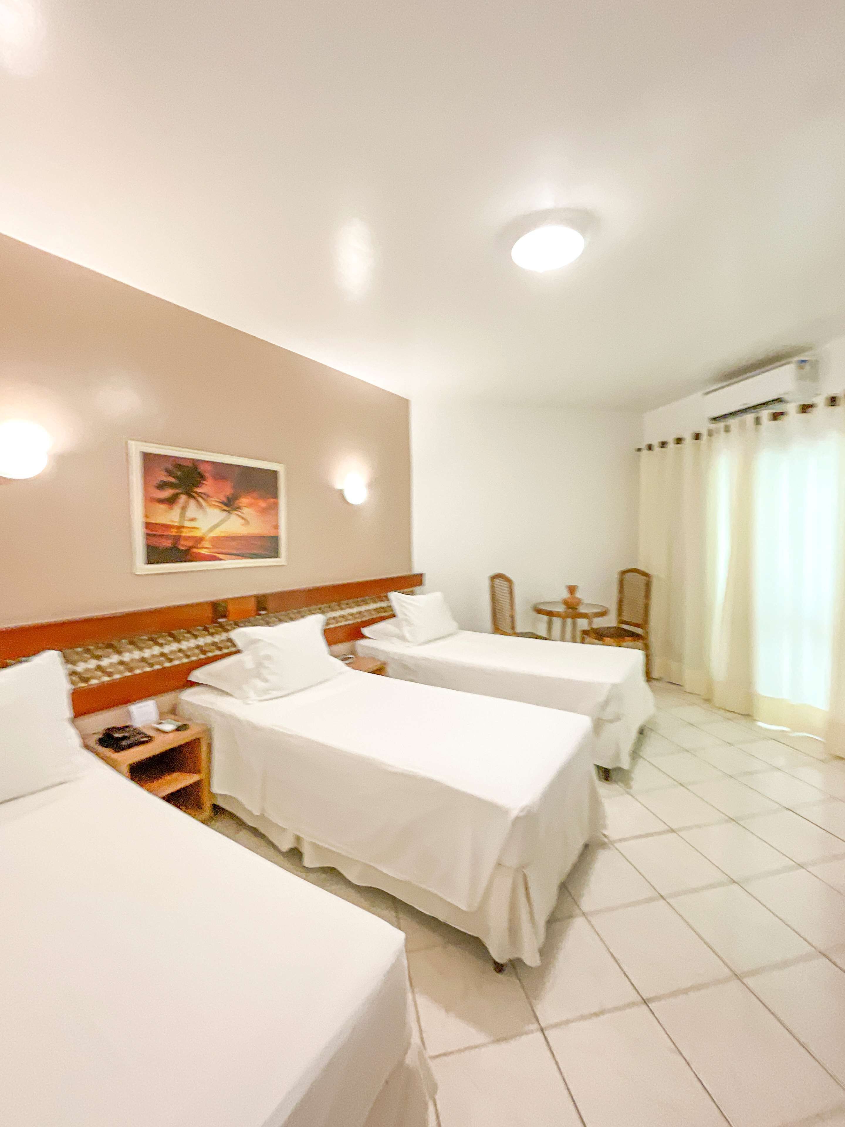A hotel room with two single beds, a small table, a chair, and a painting on the wall.