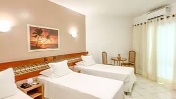 A hotel room with two single beds, a small table, a chair, and a painting on the wall.