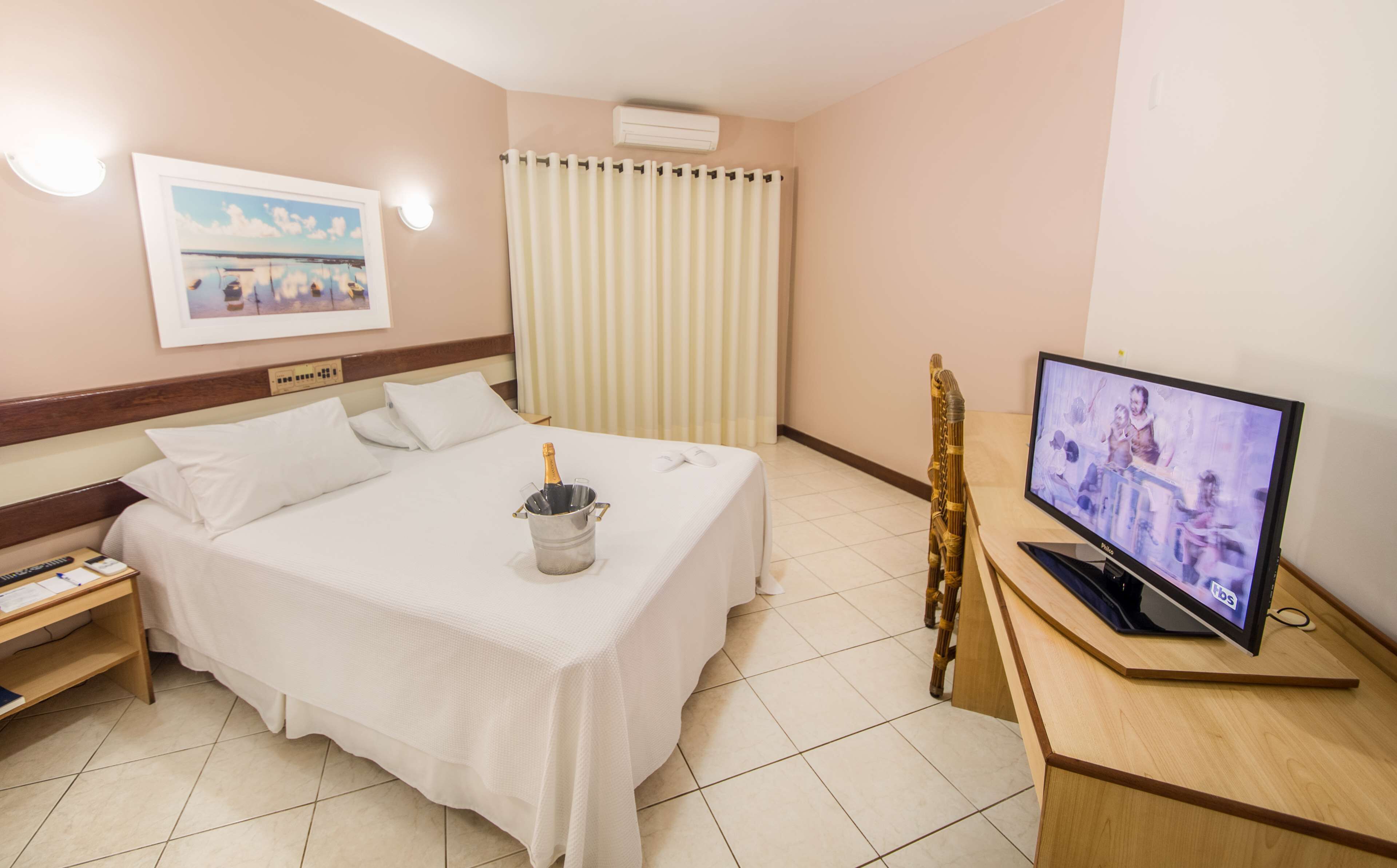 Ett hotellrum med en säng, en tv, en minibar och en tavla på väggen.