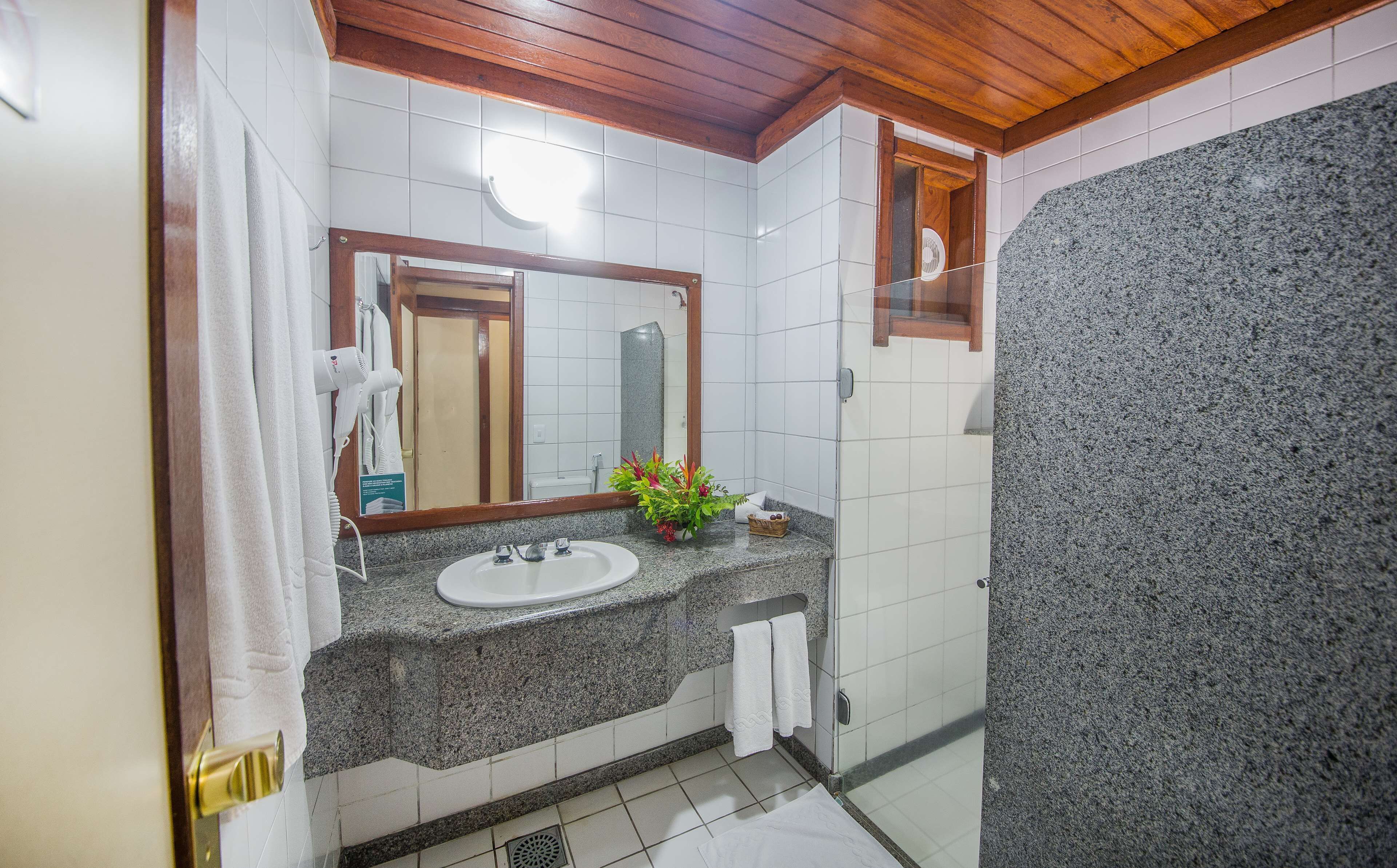 Un baño con lavamanos de encimera de granito, espejo, toallero y zona de ducha.