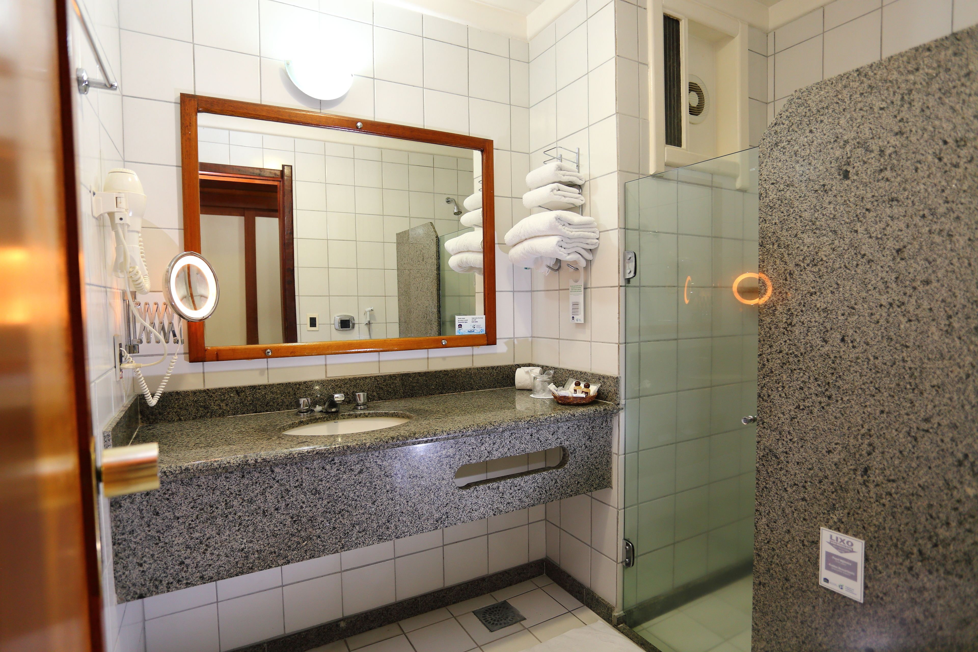 Ein Badezimmer mit Granitwaschtisch, einem Spiegel, einem Fön und einer Duschkabine aus Glas.