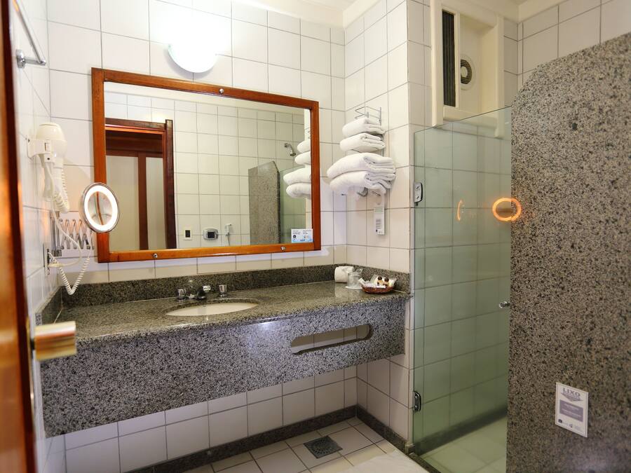 Ein Badezimmer mit Granitwaschtisch, einem Spiegel, einem Fön und einer Duschkabine aus Glas.