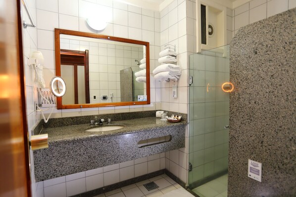 Ein Badezimmer mit Granitwaschtisch, einem Spiegel, einem Fön und einer Duschkabine aus Glas.
