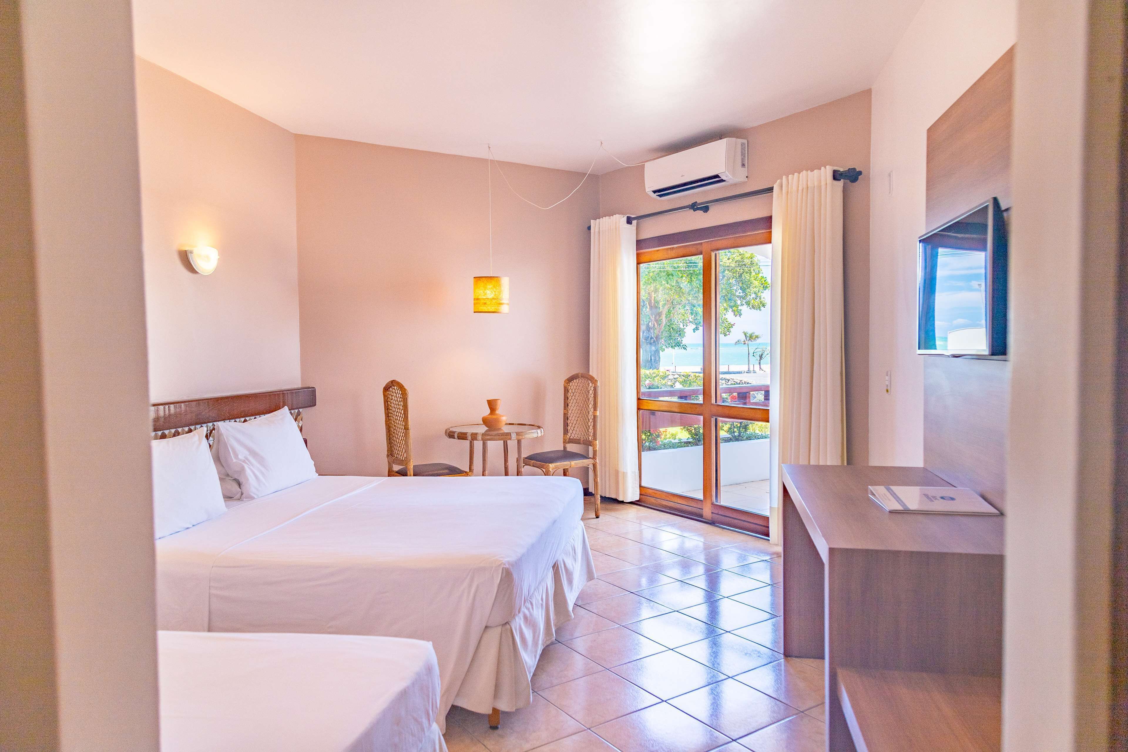 A hotel room with two beds, a small table, a chair, a desk, and a TV.