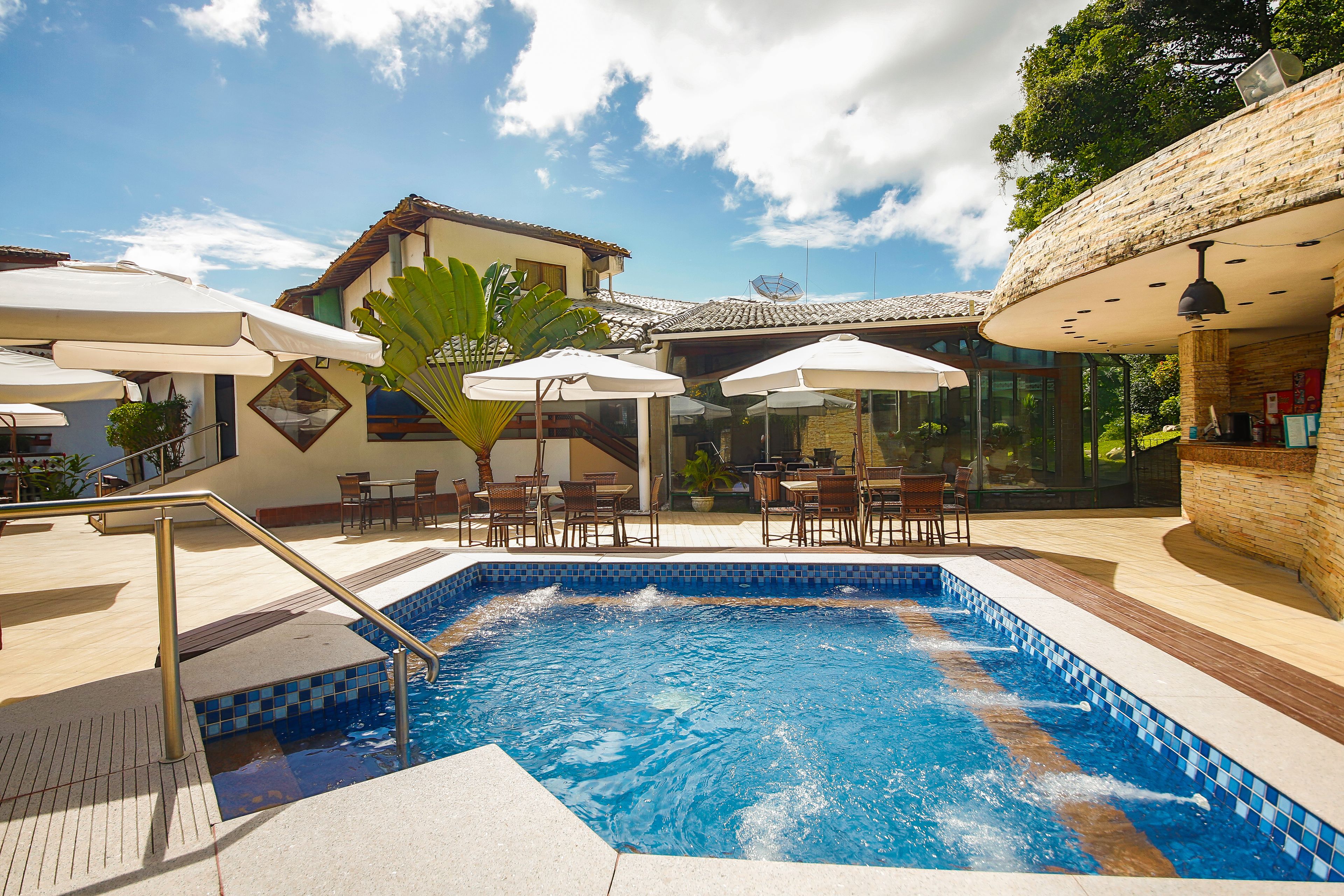 Una piscina con borde de azulejos, rodeada de mobiliario exterior y sombrillas.