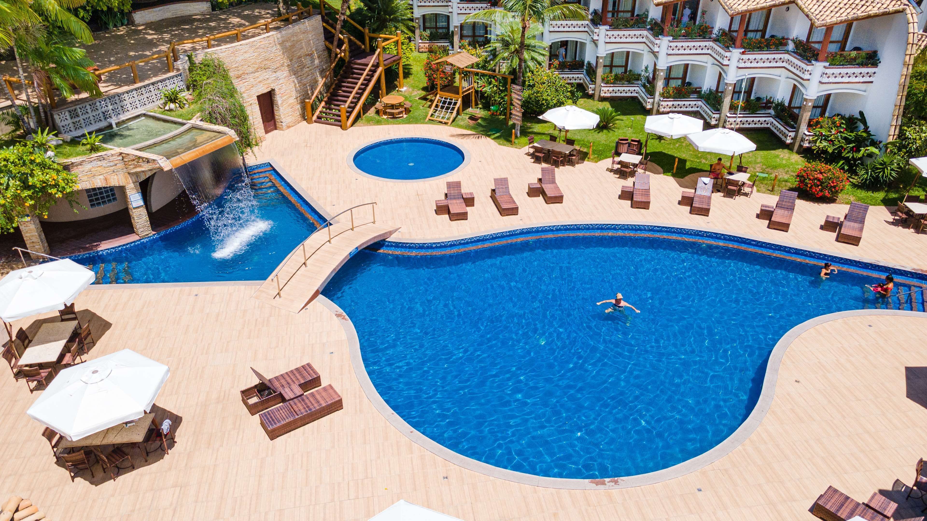 A large pool with a diving board and a smaller pool, surrounded by lounge chairs and umbrellas.