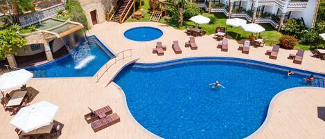 A large pool with a diving board and a smaller pool, surrounded by lounge chairs and umbrellas.