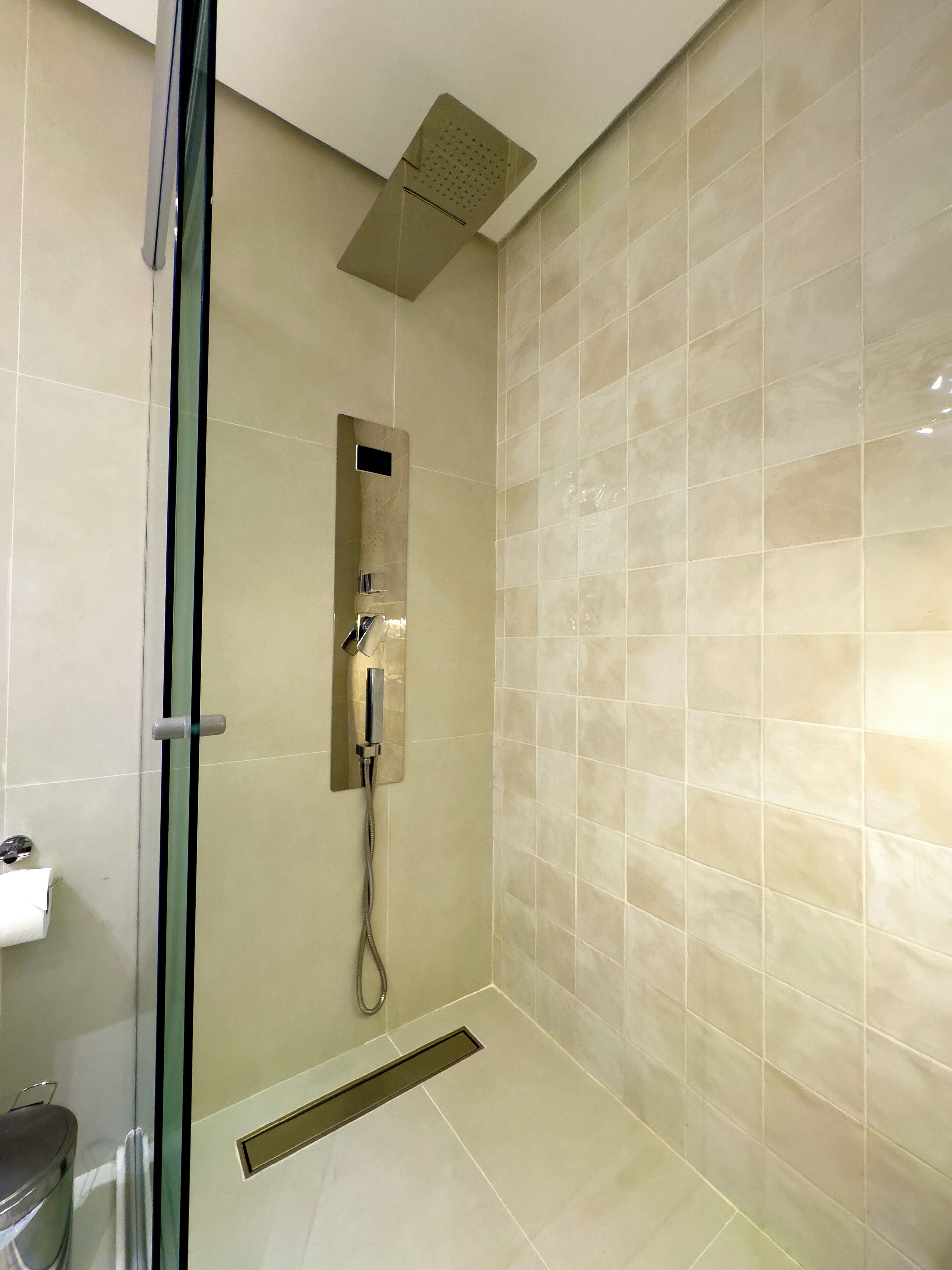 Ein modernes Badezimmer mit einer Duschkabine aus Glas, einer Handbrause und einer wandmontierten Bedienkonsole.