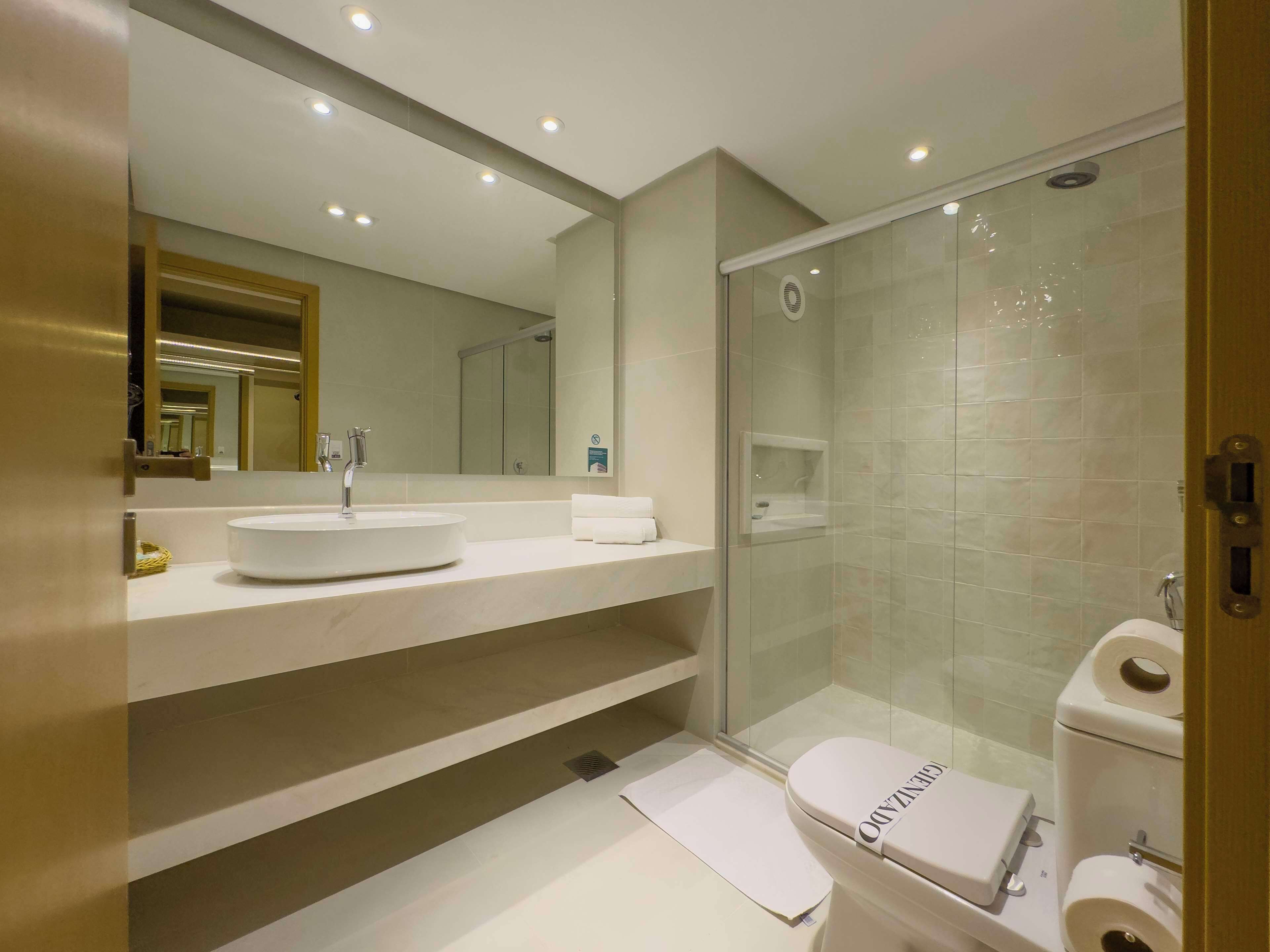 Un baño moderno con ducha envuelta en vidrio, un lavabo blanco y un inodoro con la marca visible.