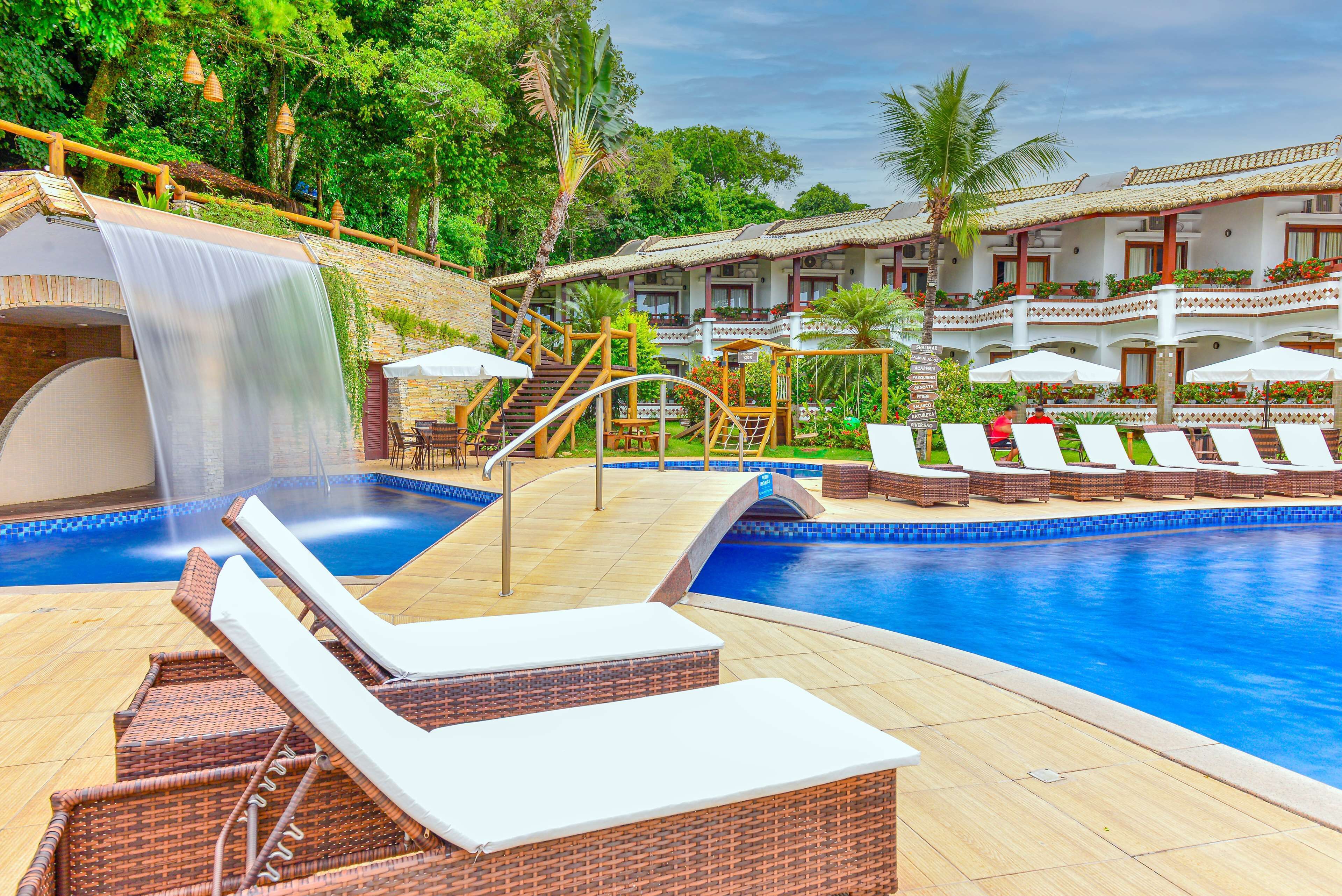 A pool area with lounge chairs, a waterfall feature, and a building with balconies.
