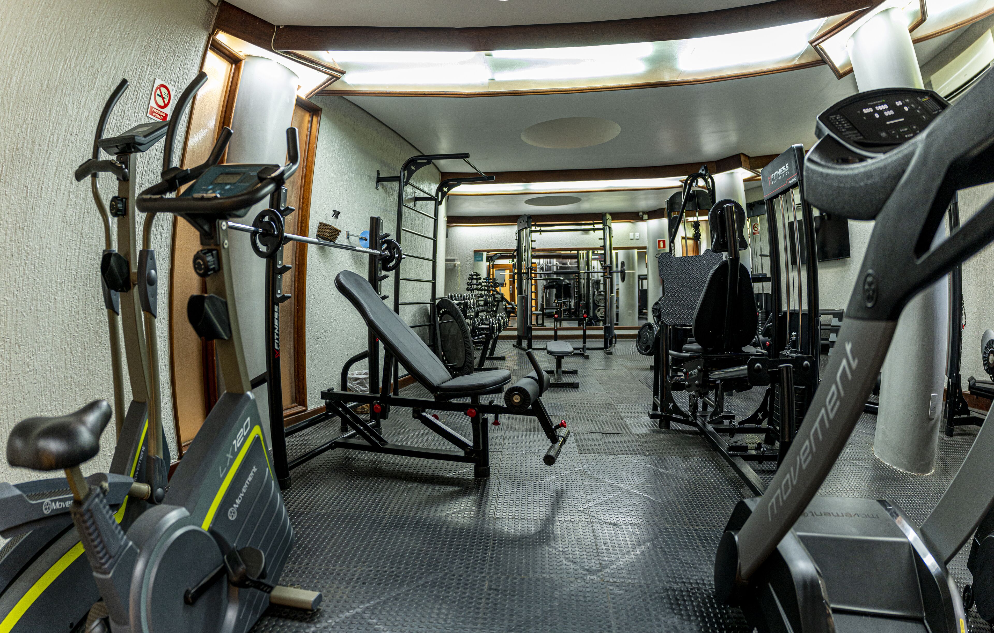 Un gimnasio con máquinas de cardio, equipo de levantamiento de pesas y un espejo grande.