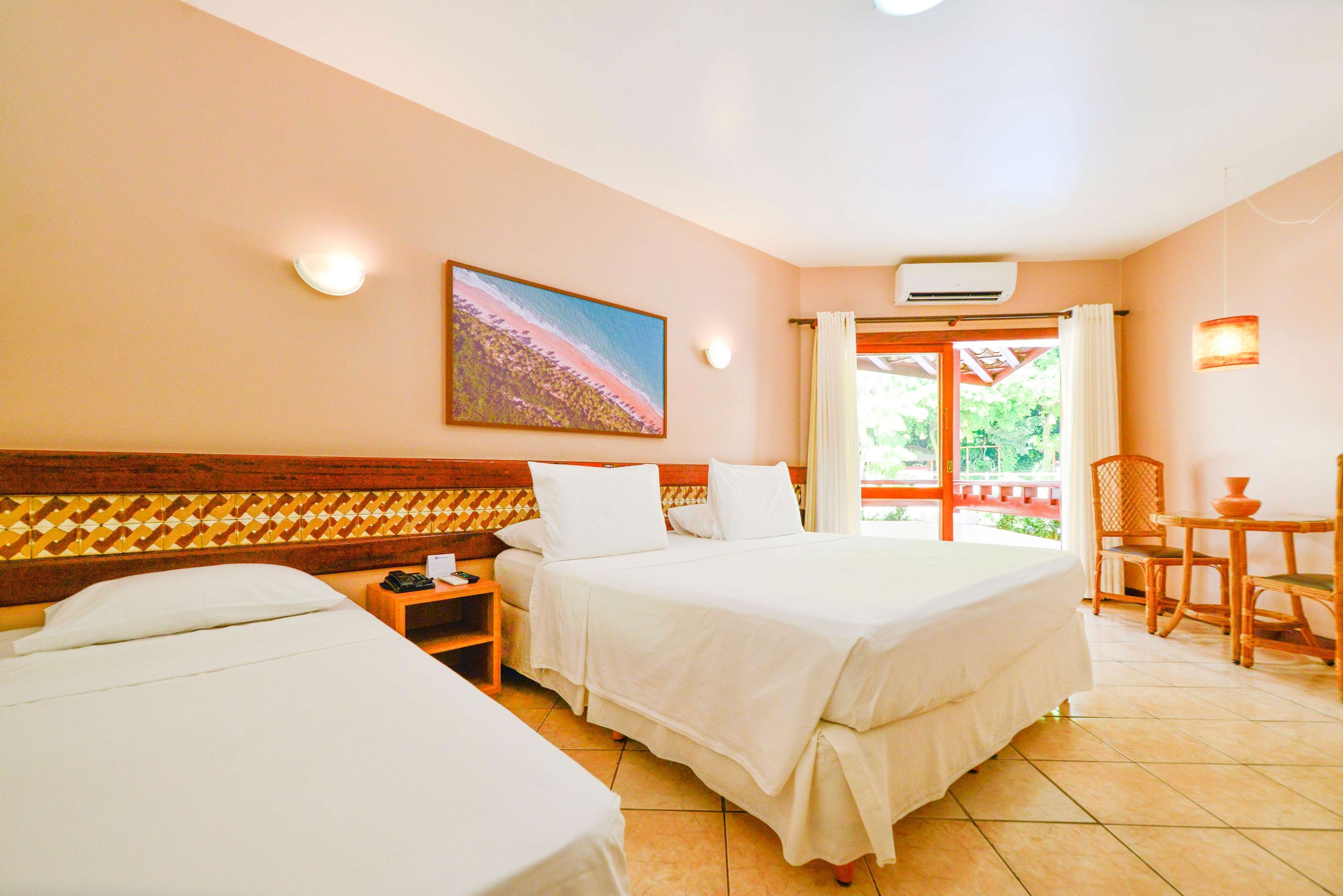 Habitación de hotel con dos camas, un cuadro en la pared, un equipo de aire acondicionado y vistas al exterior a través de una puerta de cristal.