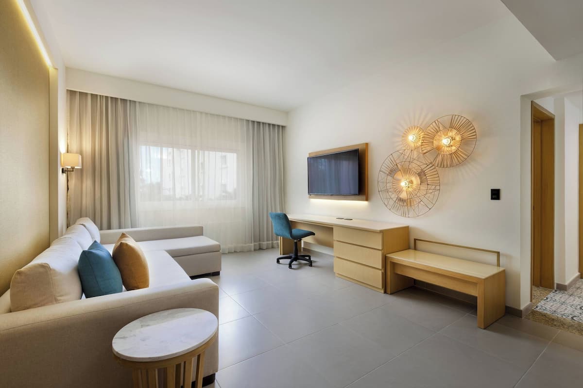 Een moderne hotelkamer met een bank, een bureau, een stoel, een televisie en decoratieve wandlampen.