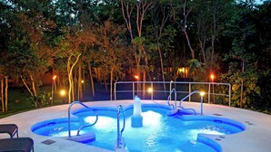 Un bain à remous avec une fontaine au centre, entouré d’une piscine et d’une rambarde en métal.