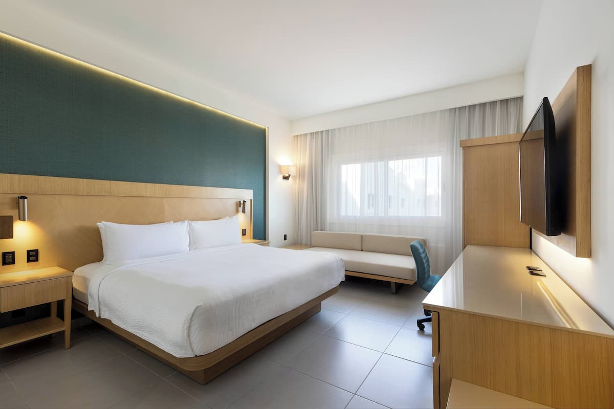 Hotelkamer met een groot bed, bureau, stoel, televisie en raam met gordijnen.