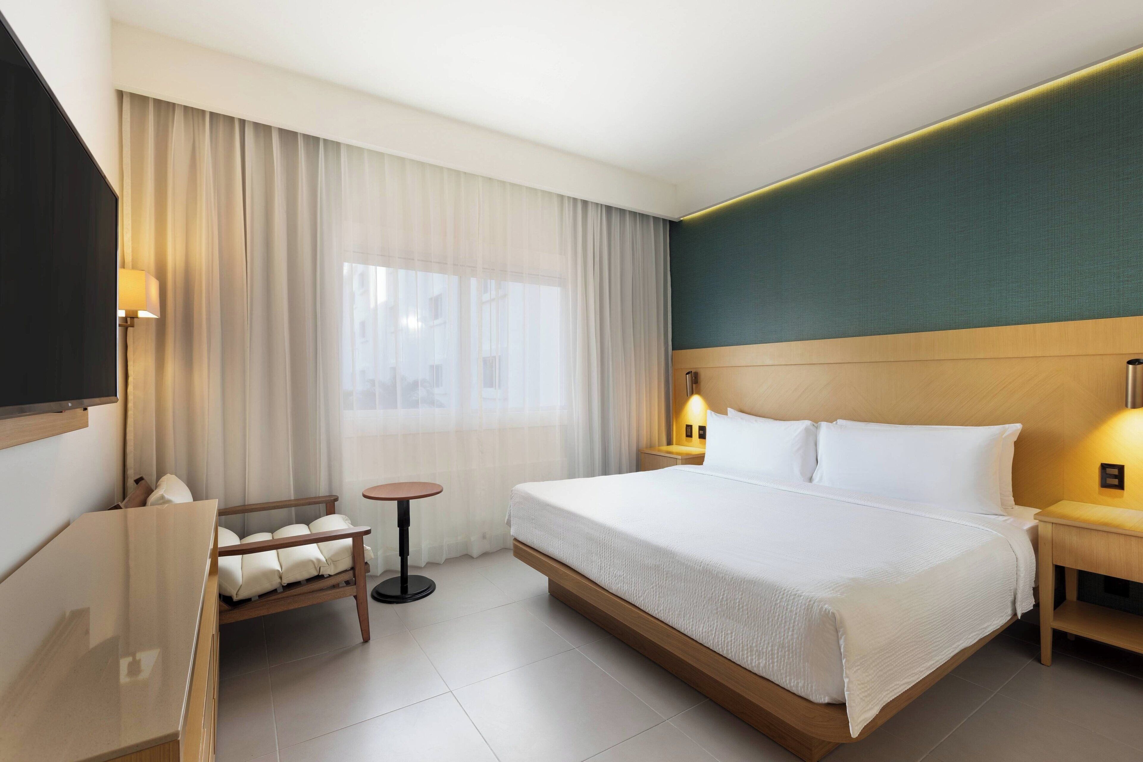 A hotel room with a large bed, a desk, a chair, and a TV.