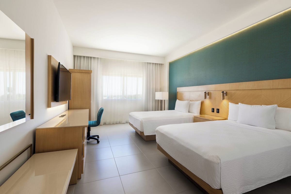 Een hotelkamer met twee bedden, een bureau, een stoel, een televisie en een raam met gordijnen.