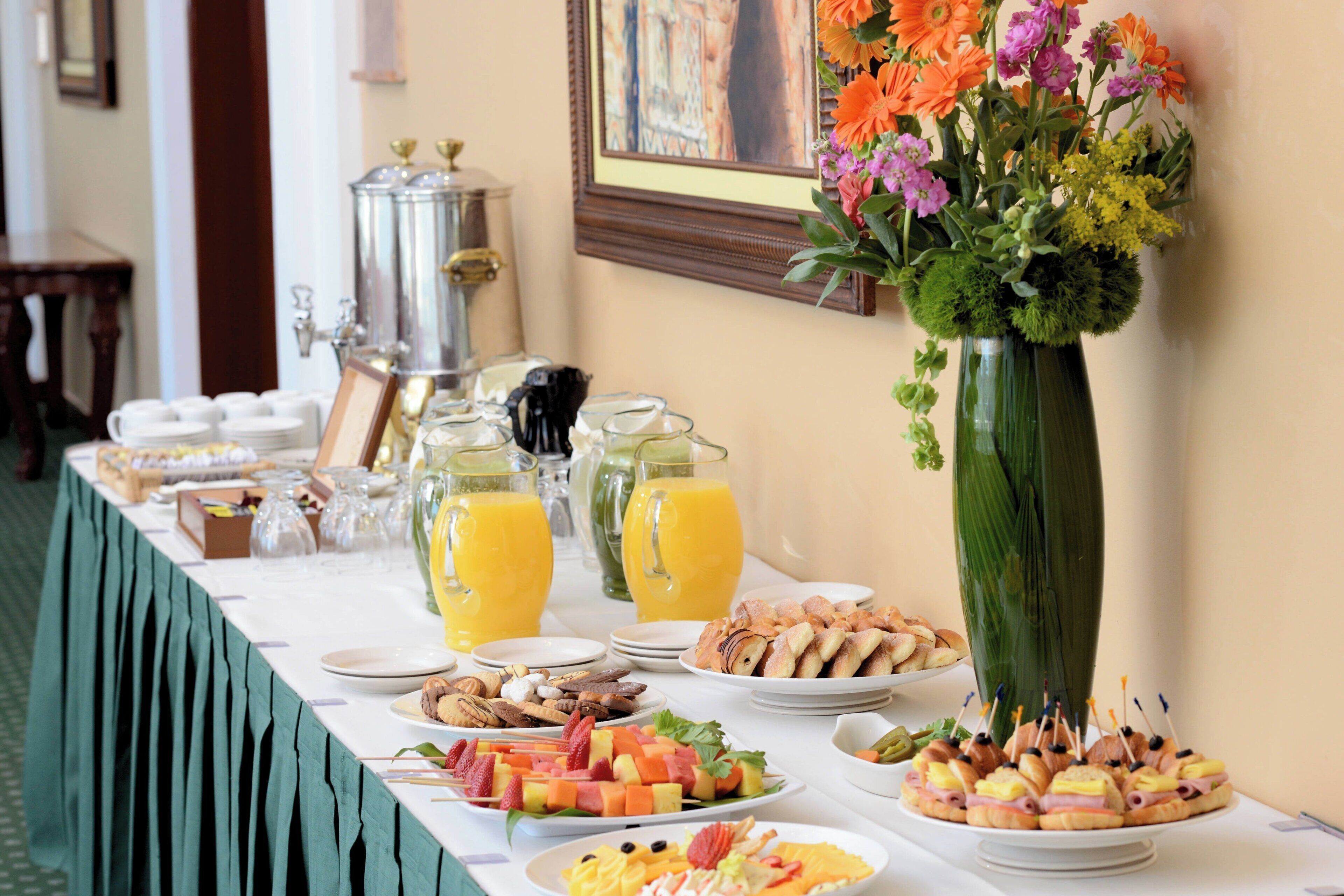 A buffet table with various food items, a large vase of flowers, and a coffee station.
